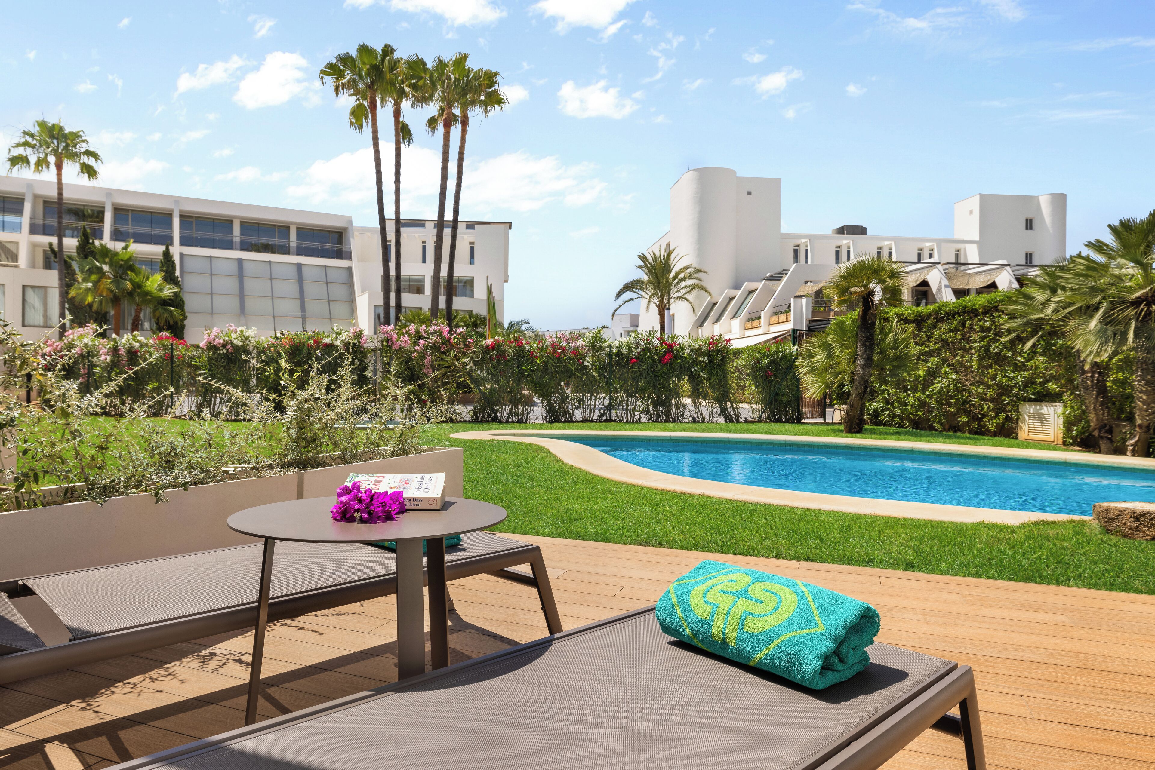 A poolside area with a lounge chair, a small table with a purple flower, and a blue towel.