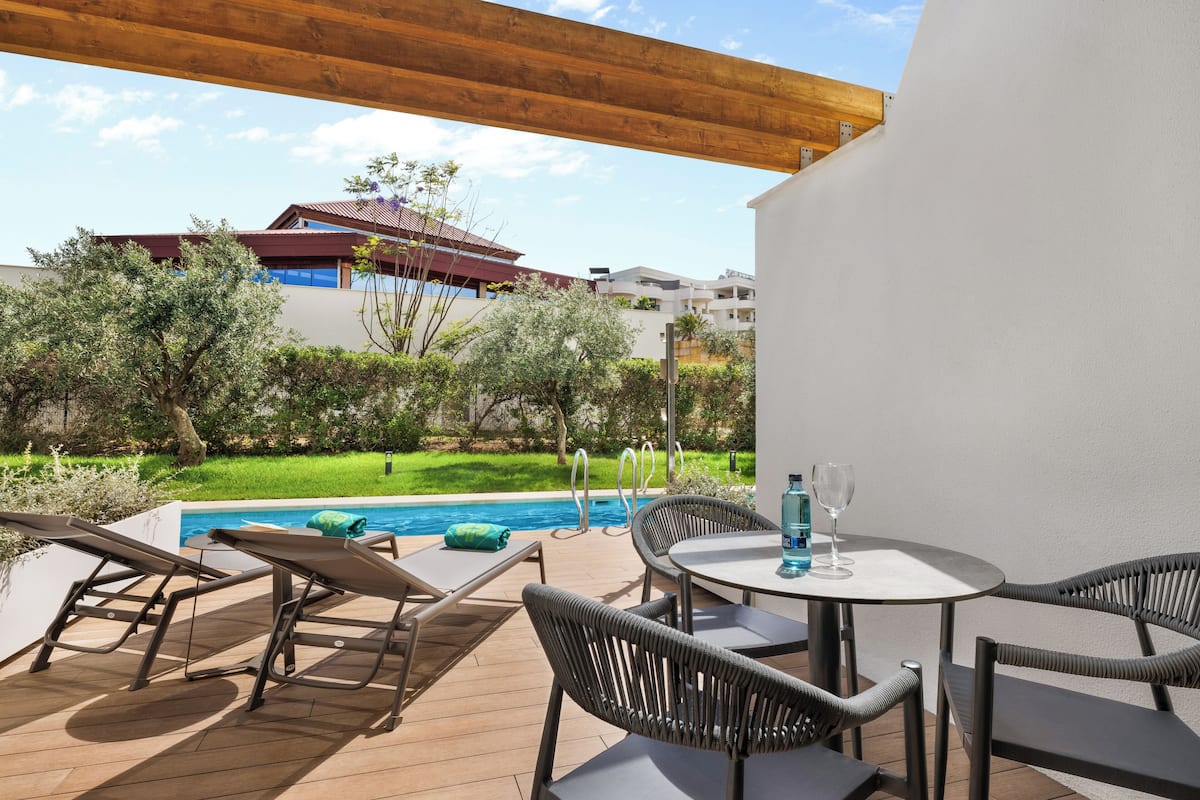A poolside area with lounge chairs, a table, and a view of a building with a red roof.