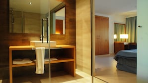 A modern bathroom with a glass shower enclosure, a wooden vanity, and a bed in the adjacent room. - Protur Palmeras Playa Hotel - All Inclusive (Sant Llorenc des Cardassar)