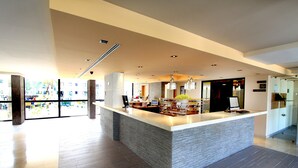 A spacious hotel lobby with a central reception desk, modern lighting fixtures, and a view of the outdoor area through large windows. - Protur Palmeras Playa Hotel - All Inclusive (Sant Llorenc des Cardassar)