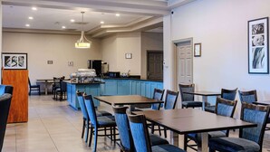 A dining area with blue chairs, wooden tables, and a kitchen in the background. - Country Inn & Suites by Radisson, BWI Airport (Baltimore), MD (Linthicum Heights)