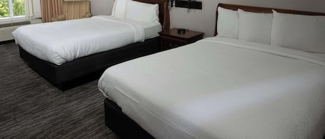 Una habitación de hotel con dos camas, una mesita de noche con lámparas y una ventana con cortinas.