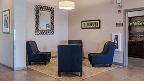 Un hall d’entrée avec trois fauteuils bleu foncé, un grand miroir et un tapis beige.
