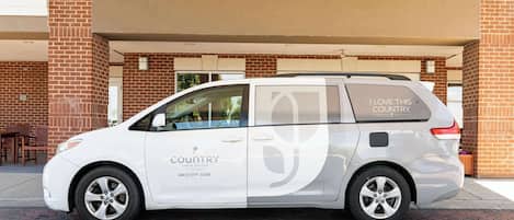 A white van parked in front of a building with a brick facade. The van has text on its side that reads "I LOVE THIS COUNTRY" and "countryinn.com".