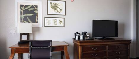 Une chambre d’hôtel comprenant un lit, un bureau avec une chaise, une télévision, une commode et des œuvres d’art encadrées accrochées au mur.