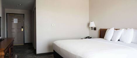 A hotel room with a large bed, a desk, a lamp, and a door leading to another room.