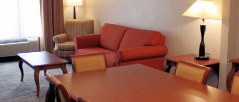 Habitación de hotel con una mesa de comedor, dos sillas, un sofá, una lámpara y una ventana con cortinas.