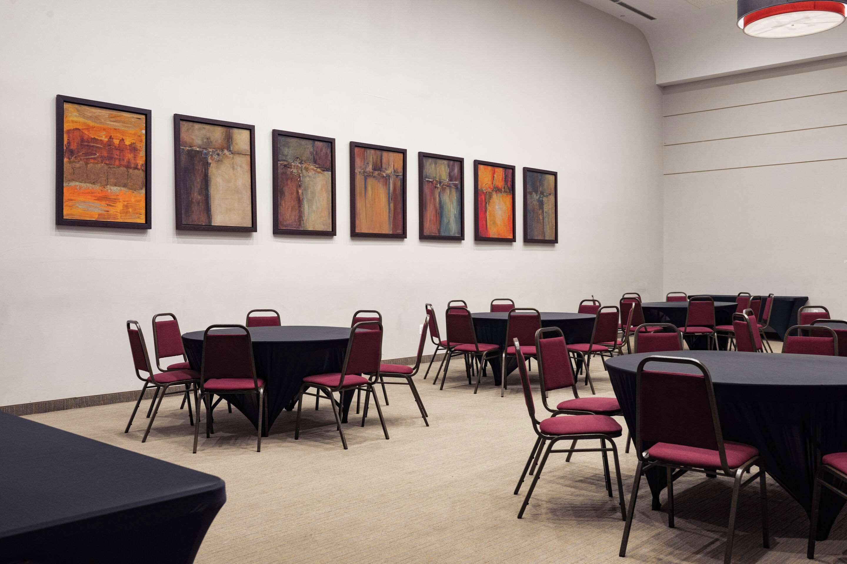A conference room with tables and chairs, framed artwork on the wall, and a modern ceiling light.
