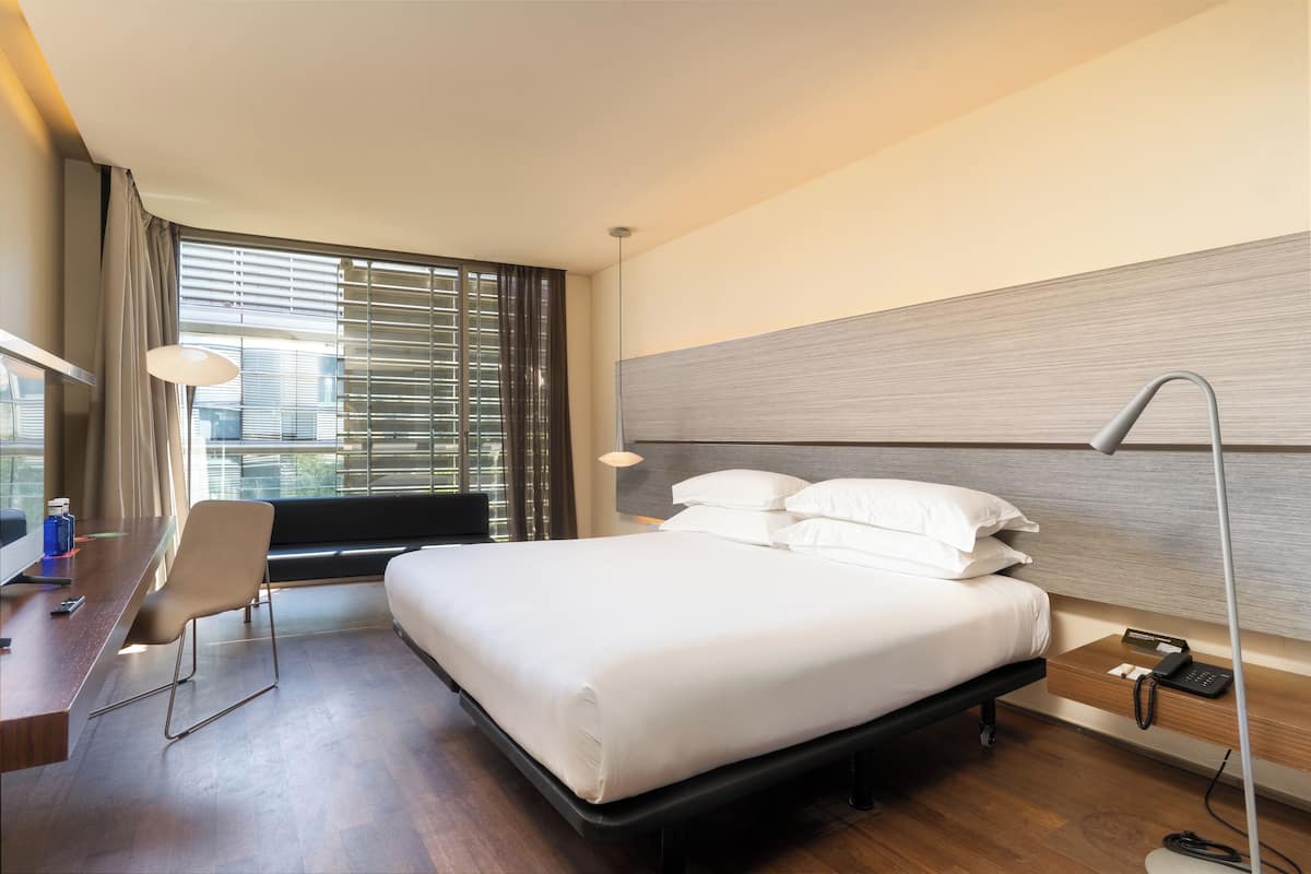 A modern hotel room with a large bed, a desk, and a chair.