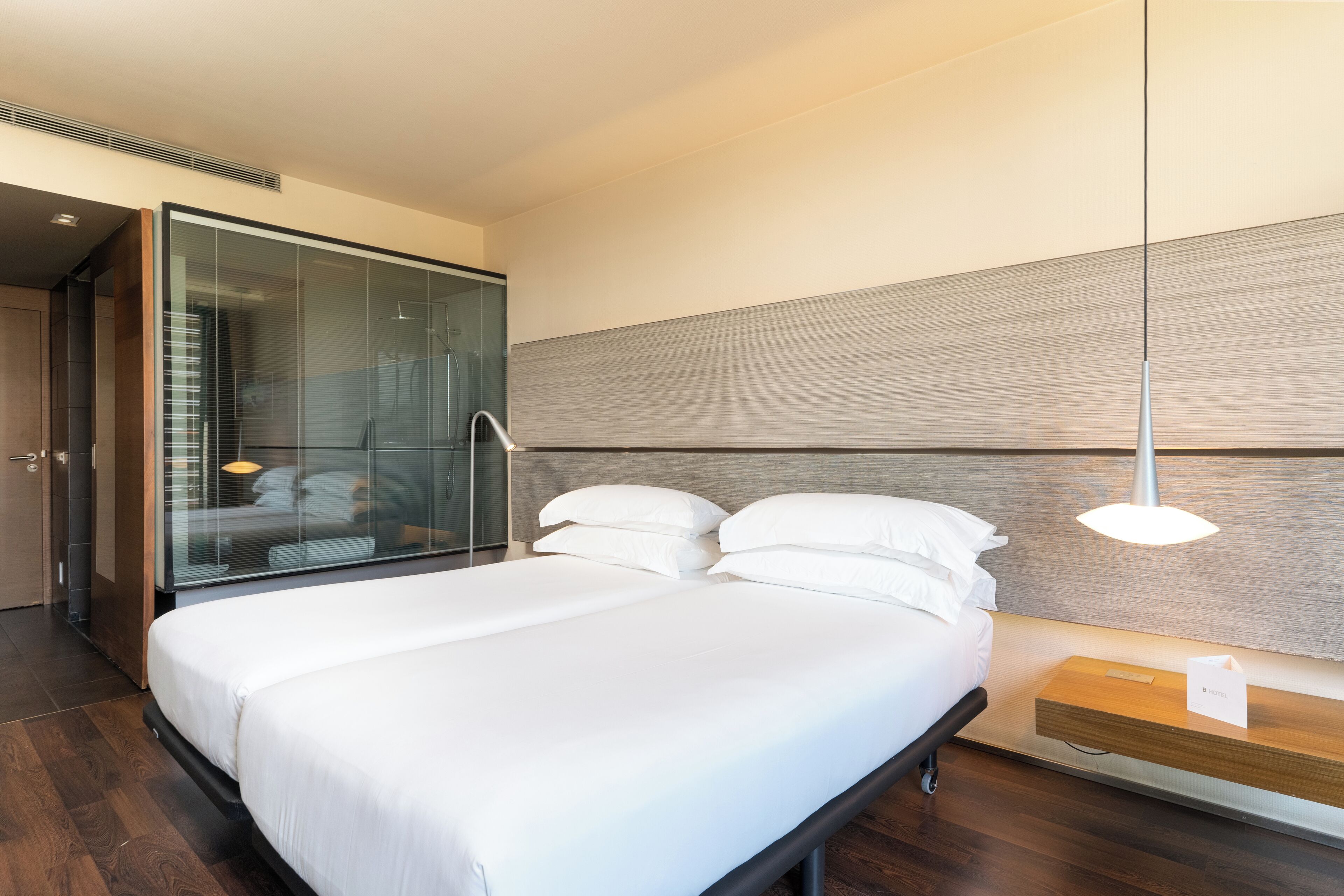 Una habitación de hotel moderna con una cama grande, cabecera de madera y separador de vidrio.