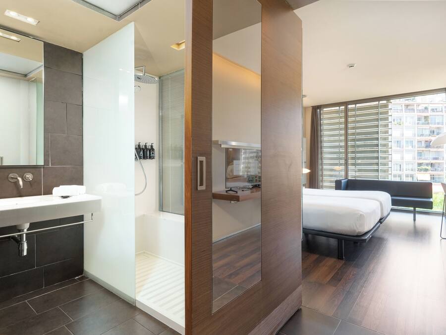 Una habitación de hotel moderna con un espejo grande, una ducha, una cama y una mesita de noche.