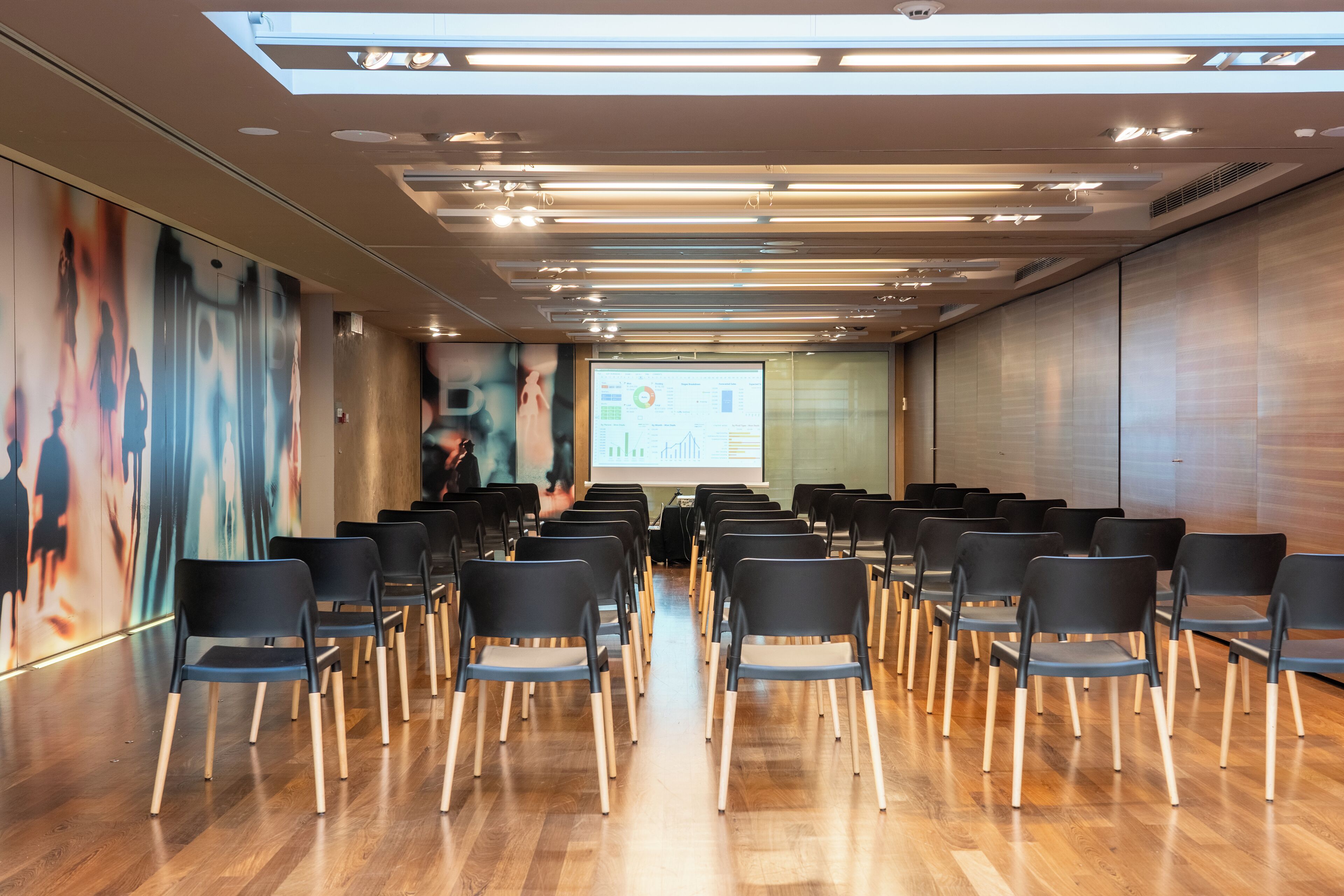 A conference room with rows of chairs, a projector screen, and a presentation on the wall.