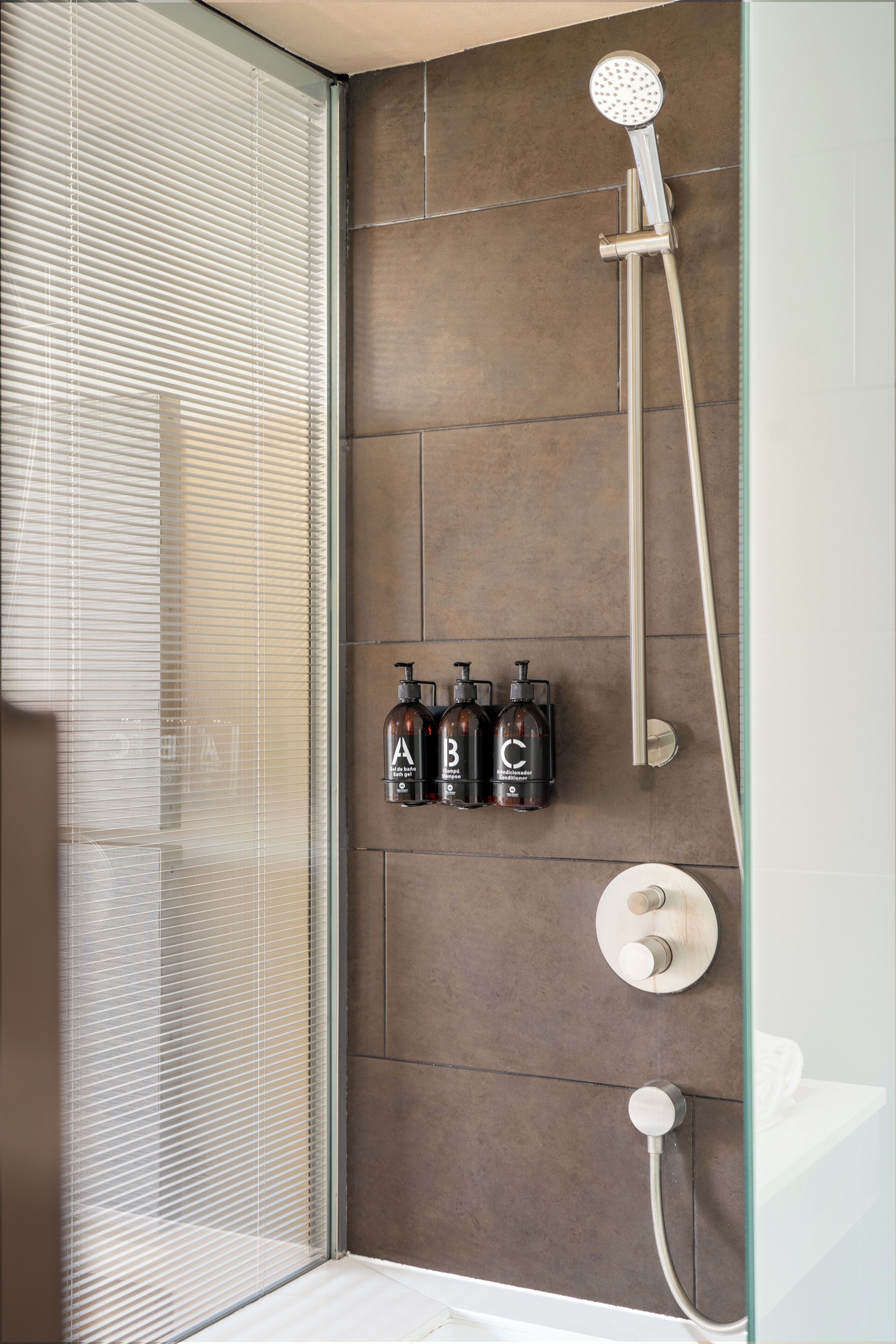 A shower with a handheld showerhead, a wall-mounted faucet, and three bottles labeled A, B, and C.