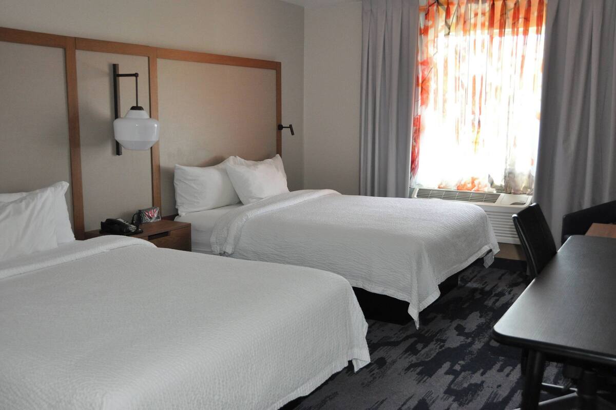 Een hotelkamer met twee bedden, een bureau, een stoel, een nachtkastje en een raam met gordijnen.