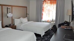 Ein Hotelzimmer mit zwei Betten, einem Schreibtisch, einem Stuhl, einem Fernseher und einem Fenster mit Vorhängen.