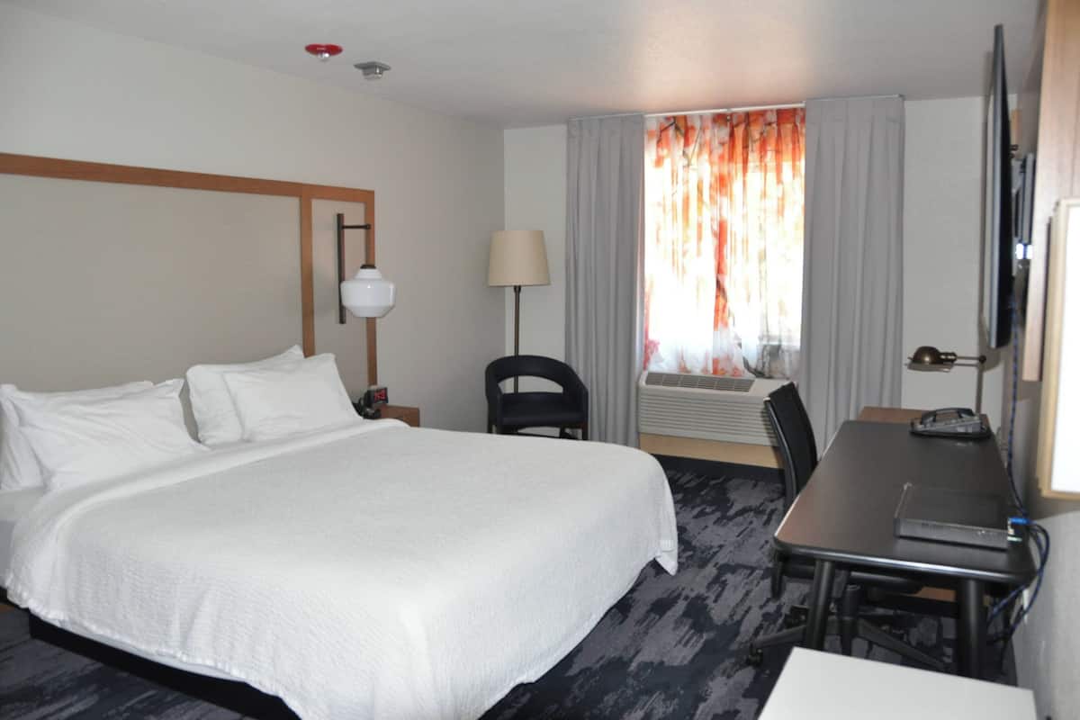 Een hotelkamer met een groot bed, een bureau, een stoel, een televisie en een raam met gordijnen.
