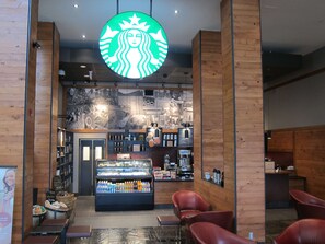 A Starbucks coffee shop interior with seating, a display case, and a wall with images. - Coast Hotel & Convention Centre Langley City (Langley)