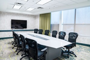 A conference room with a long table, black chairs, a flat-screen TV, and large windows with curtains. - Coast Hotel & Convention Centre Langley City (Langley)