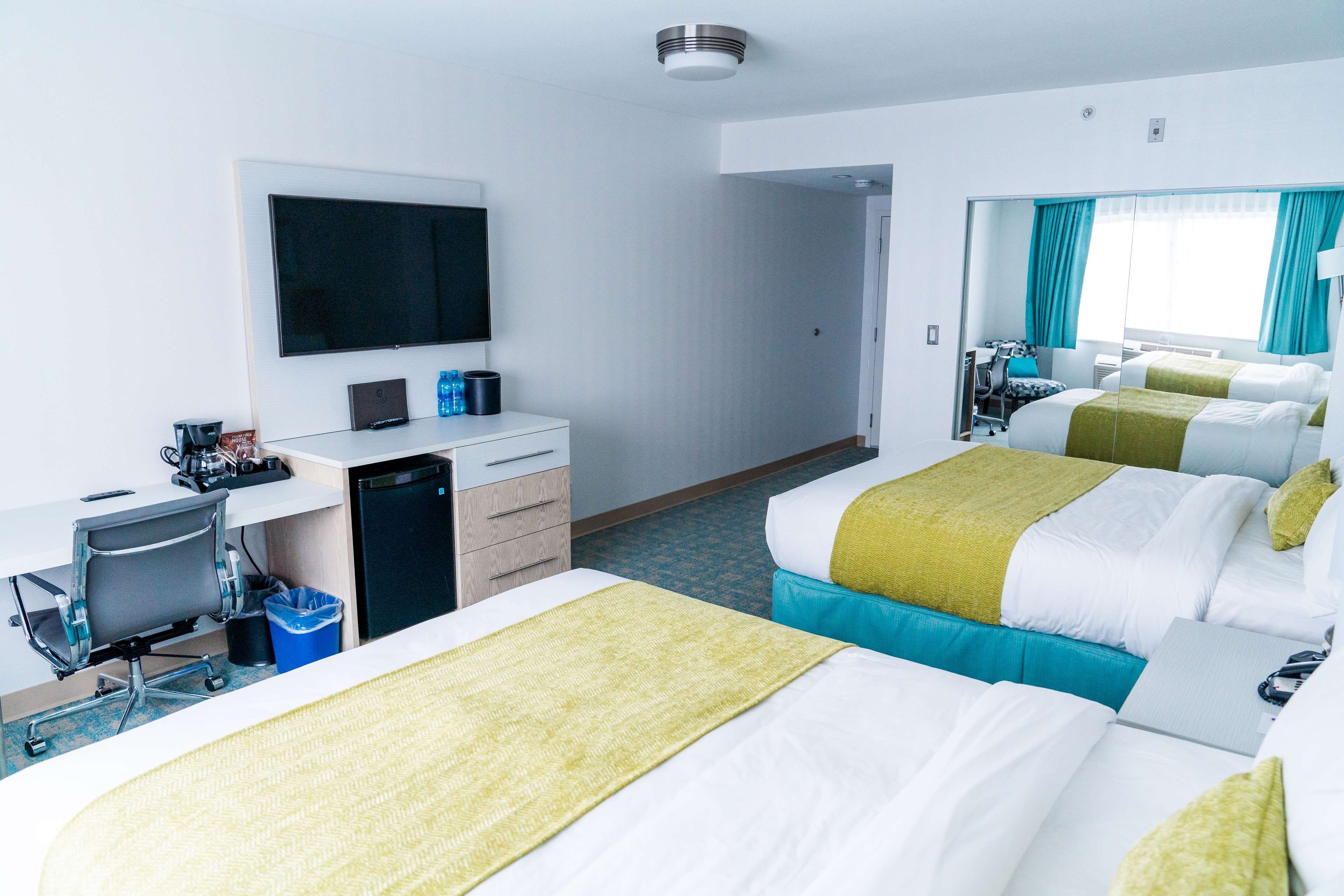 Habitación de hotel con dos camas, un escritorio, una silla, un televisor y una pequeña kitchenette.