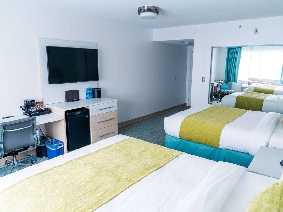 Habitación de hotel con dos camas, un escritorio, una silla, un televisor y una pequeña kitchenette.