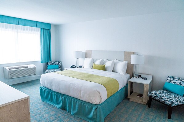 Habitación de hotel con cama, mesitas de noche, escritorio y ventana con cortinas.