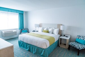 Ein Hotelzimmer mit Bett, Nachttischen, Schreibtisch und einem fenster mit Vorhängen.