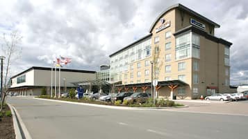 A hotel with a modern design, featuring a large parking lot and a covered walkway.