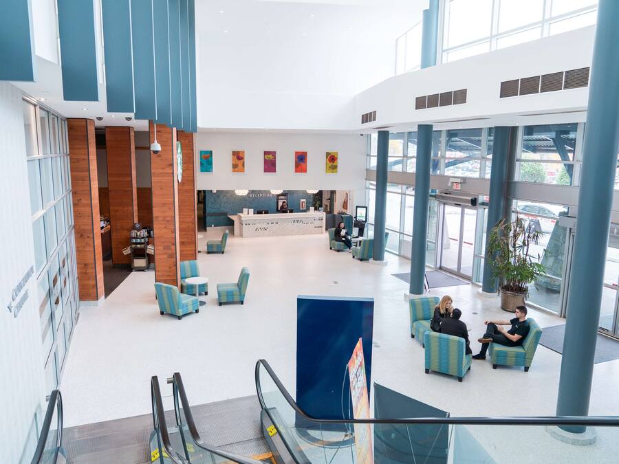 Um hall amplo com balcão de recepção, área de estar e vista para o exterior através de grandes janelas.