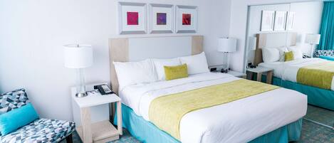 A hotel room with a large bed, a bedside table with a lamp, a chair, and a small desk with a phone.