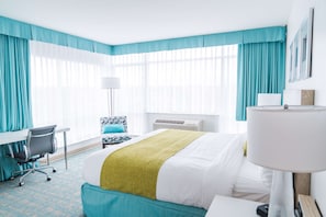 A hotel room with a bed, a desk, a chair, a lamp, and large windows with curtains. - Coast Hotel & Convention Centre Langley City (Langley)