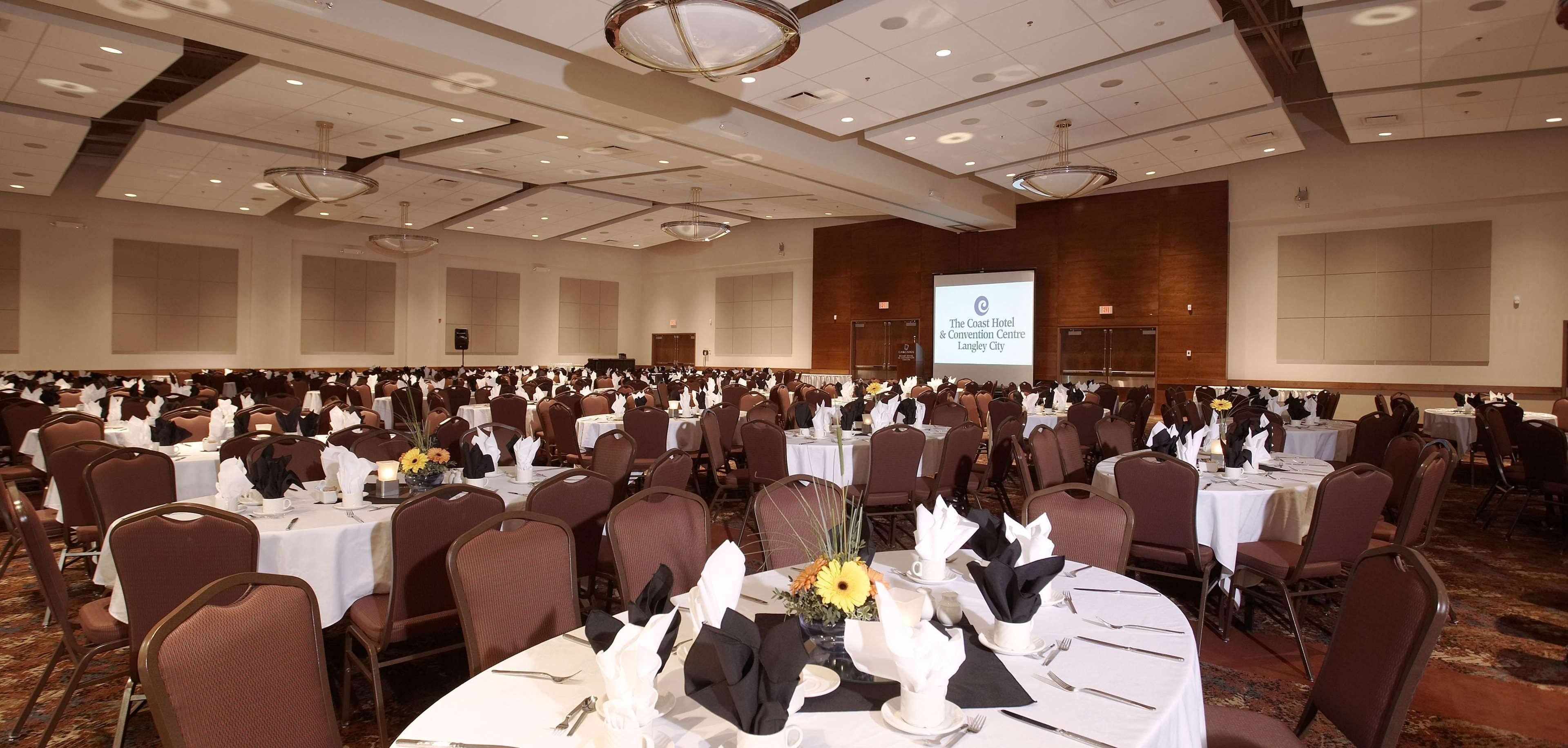 A large banquet hall with round tables, chairs, and a projection screen displaying the hotel's name.