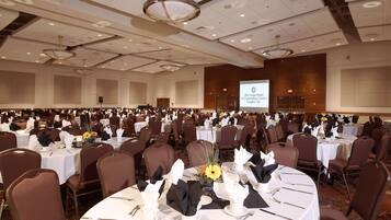 A large banquet hall with round tables, chairs, and a projection screen displaying the hotel's name.
