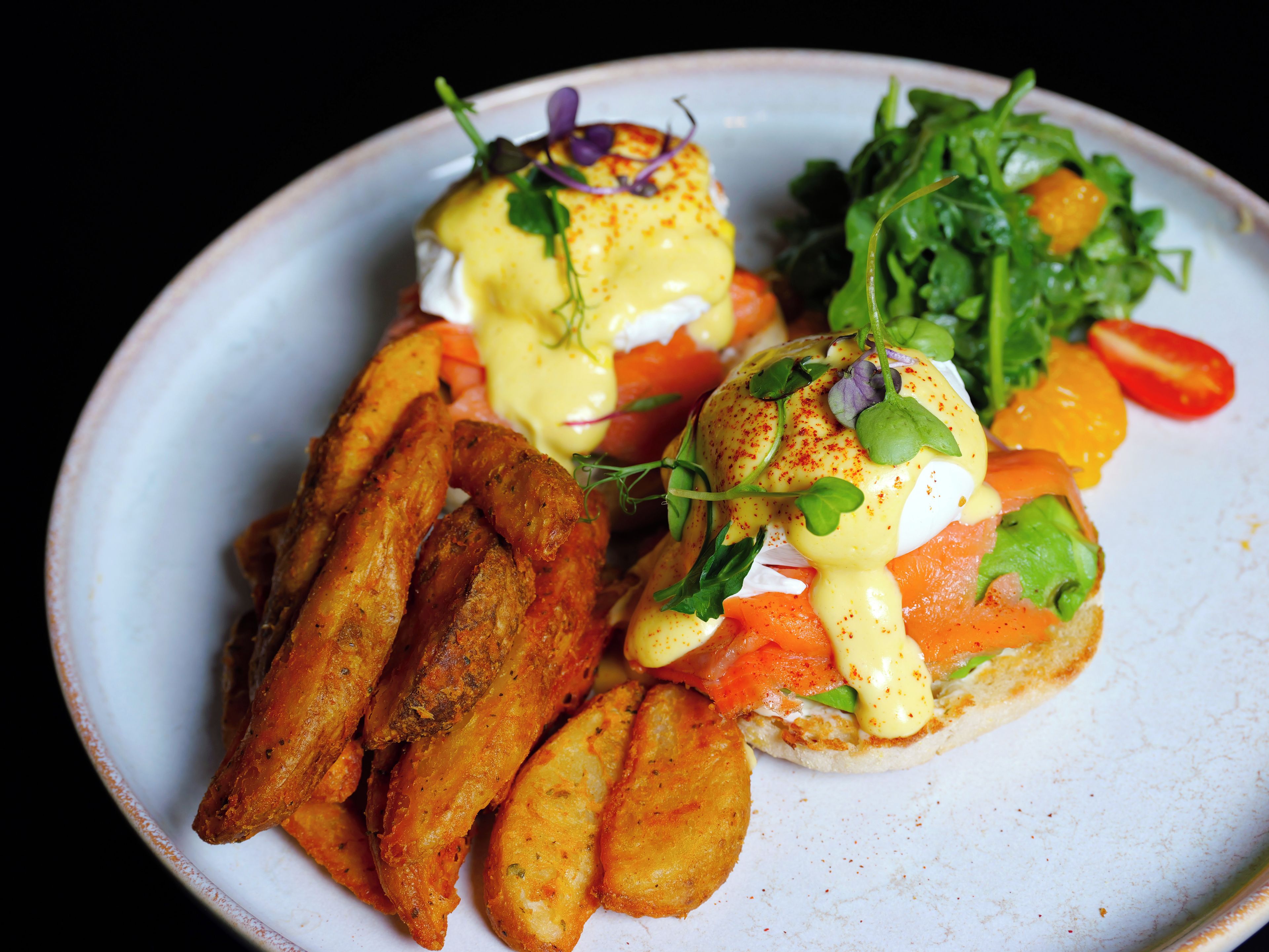 A plate of food with eggs benedict, smoked salmon, and a side of roasted potatoes.