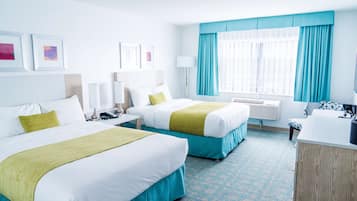 A hotel room with two beds, a desk, a chair, a small table, a lamp, and a window with curtains.