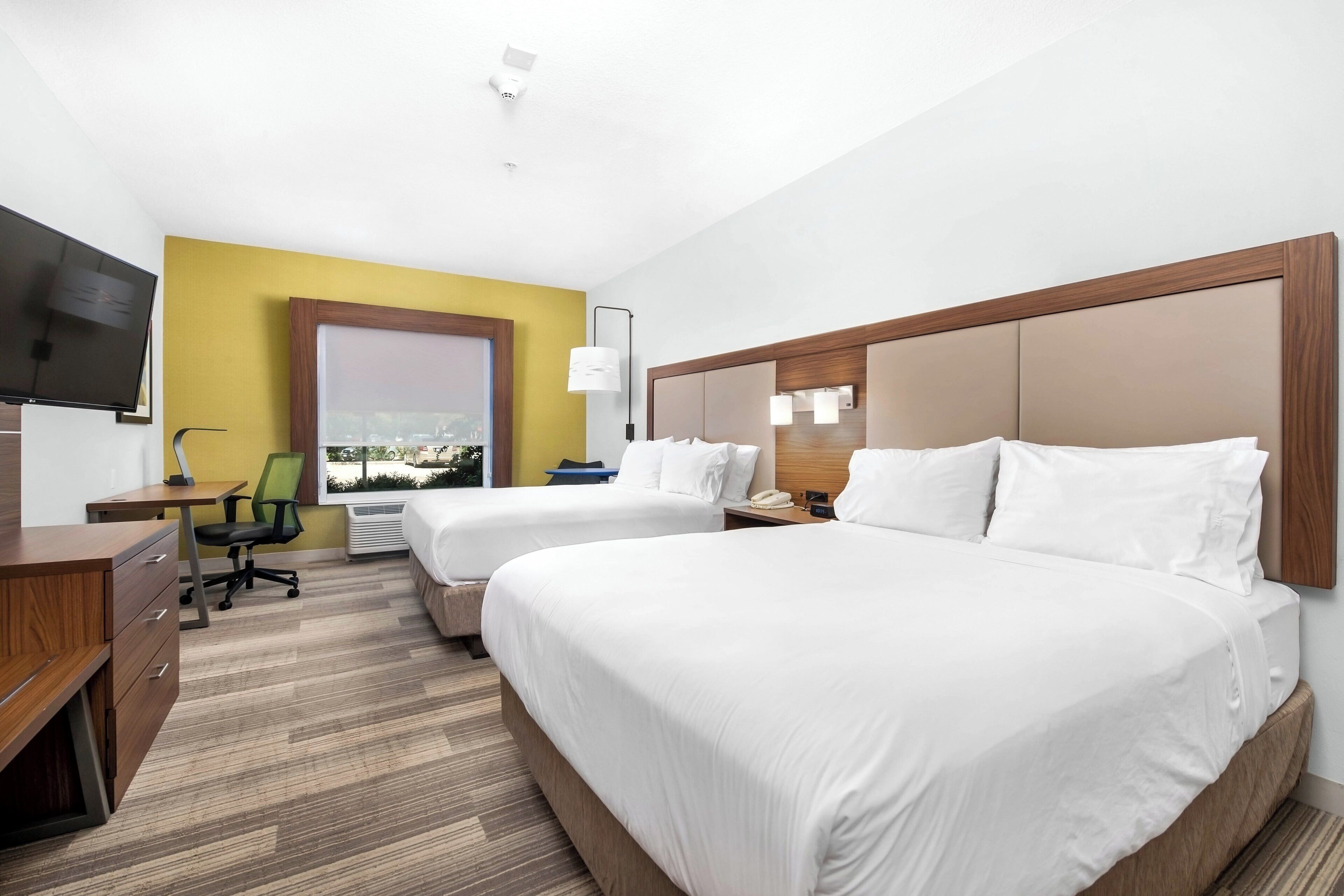 A hotel room with two beds, a desk, a chair, a TV, and a window with a view.