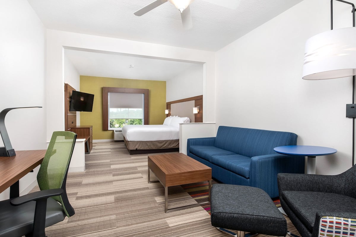 A hotel room with a bed, a blue sofa, a desk with a chair, a small table, and a TV mounted on the wall.