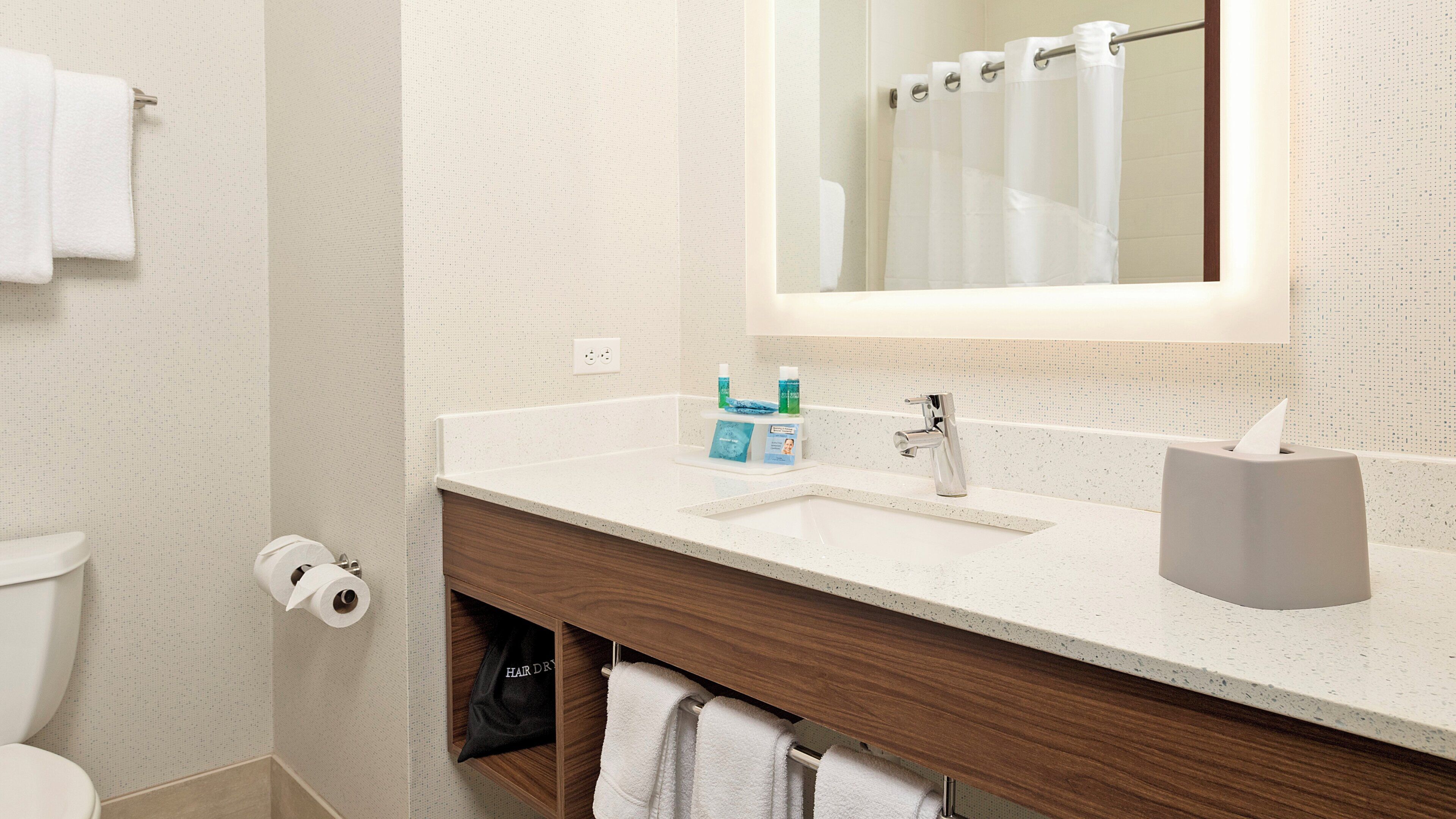 A bathroom with a white countertop, a wooden vanity, a mirror, a towel rack, and a toilet.
