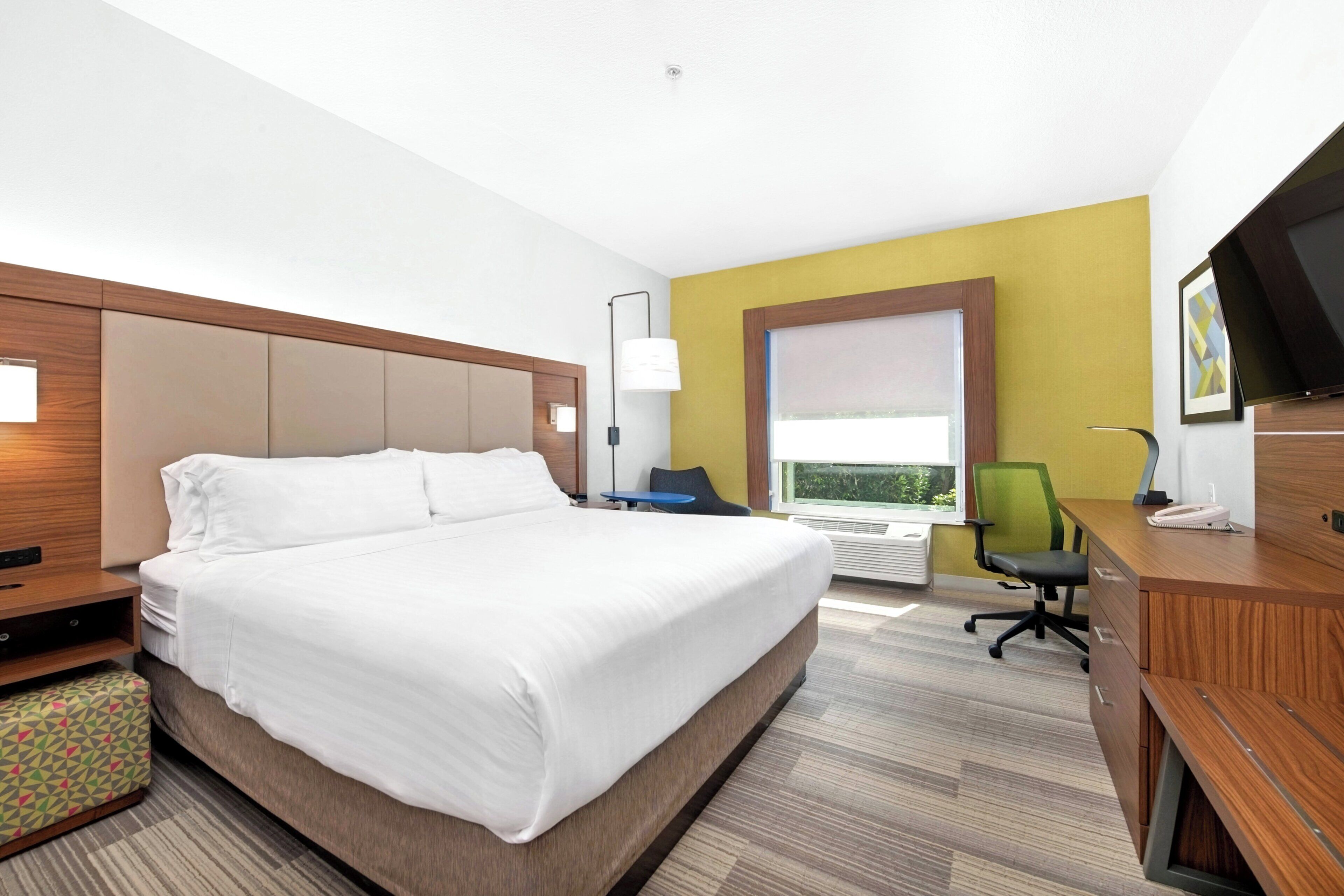 Habitación de hotel con una cama grande, un escritorio, una silla, un televisor y una ventana con vistas.