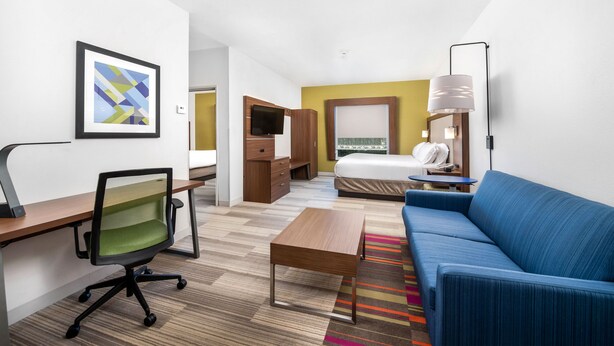 A hotel room with a bed, a blue sofa, a desk with a chair, a television, and a framed picture on the wall. - Holiday Inn Express Hotel & Suites Conroe I-45 North by IHG (Conroe)
