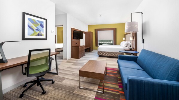 A hotel room with a bed, a blue sofa, a desk with a chair, a television, and a framed picture on the wall. - Holiday Inn Express Hotel & Suites Conroe I-45 North by IHG (Conroe)