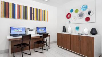 Un espacio de oficina moderno con dos escritorios, sillas, una impresora y un armario con platos decorativos.