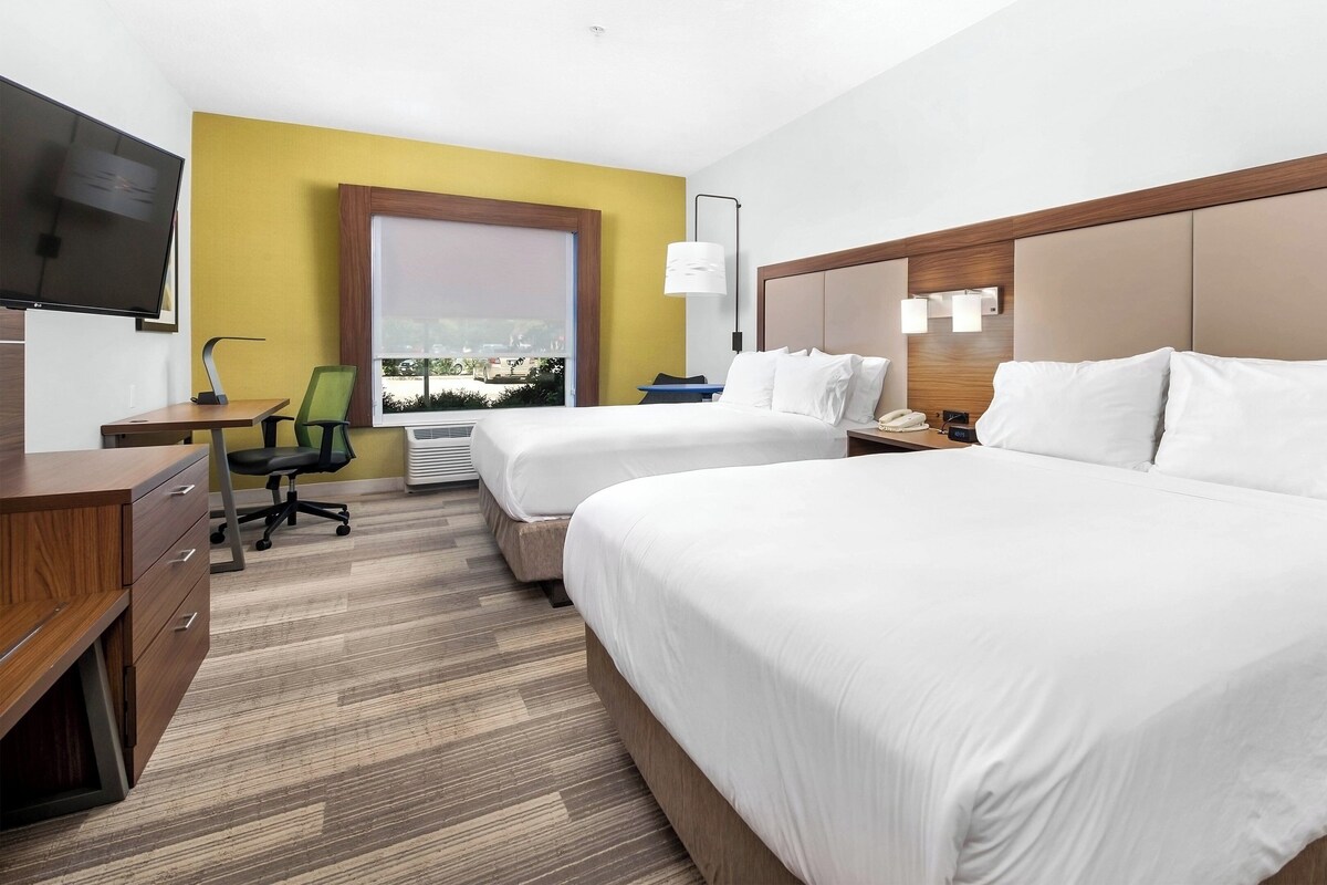 A hotel room with two beds, a desk, a chair, a TV, and a window with a view.