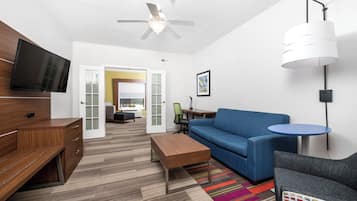A modern hotel room with a television, a ceiling fan, a sofa, a coffee table, a desk, and a chair.