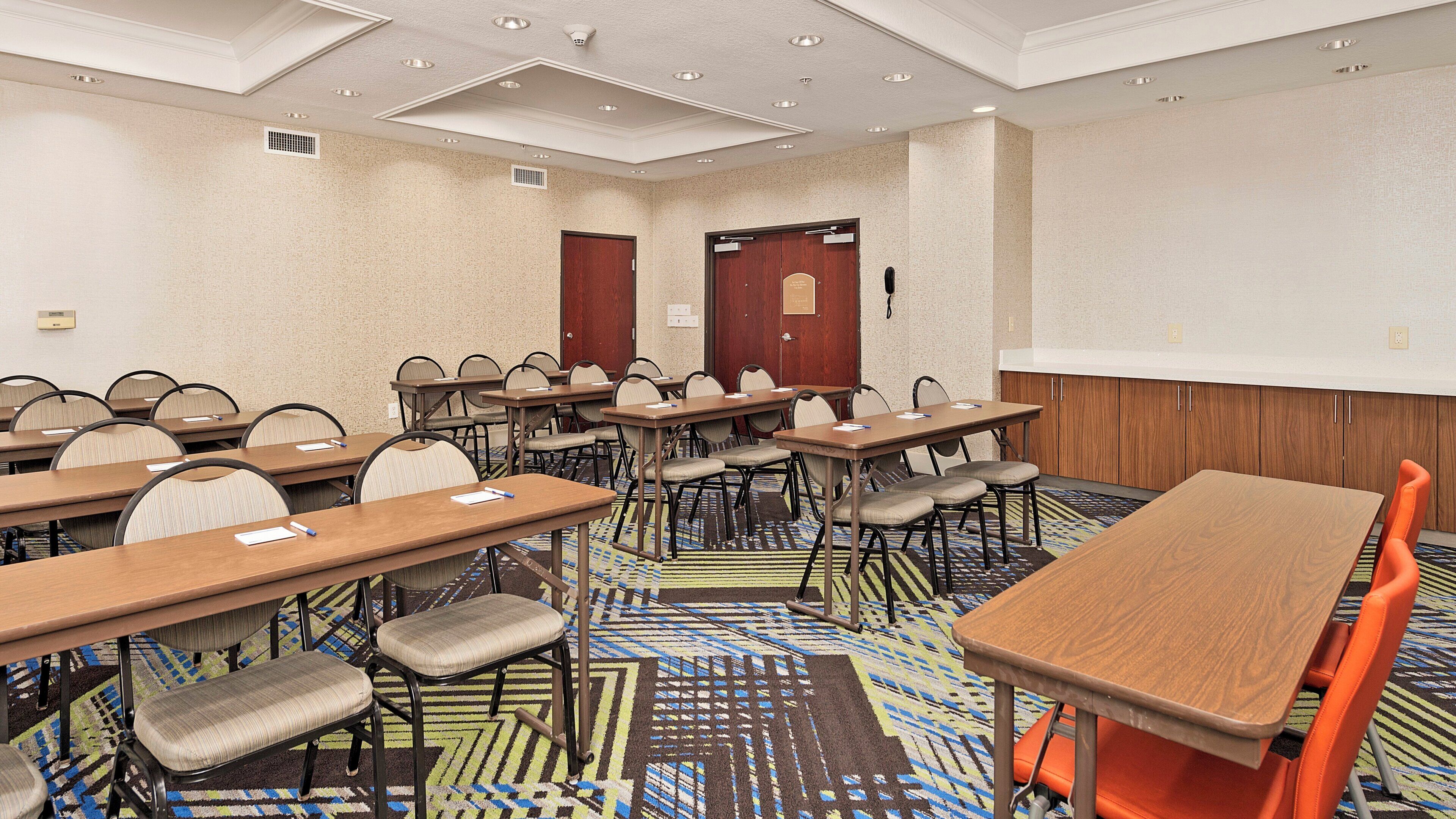 A conference room with multiple tables and chairs, a carpeted floor, and a projector screen on the wall.