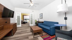 A modern hotel room with a flat-screen TV, a ceiling fan, a sofa, a coffee table, a desk, and a chair. - Holiday Inn Express Hotel & Suites Conroe I-45 North by IHG (Conroe)