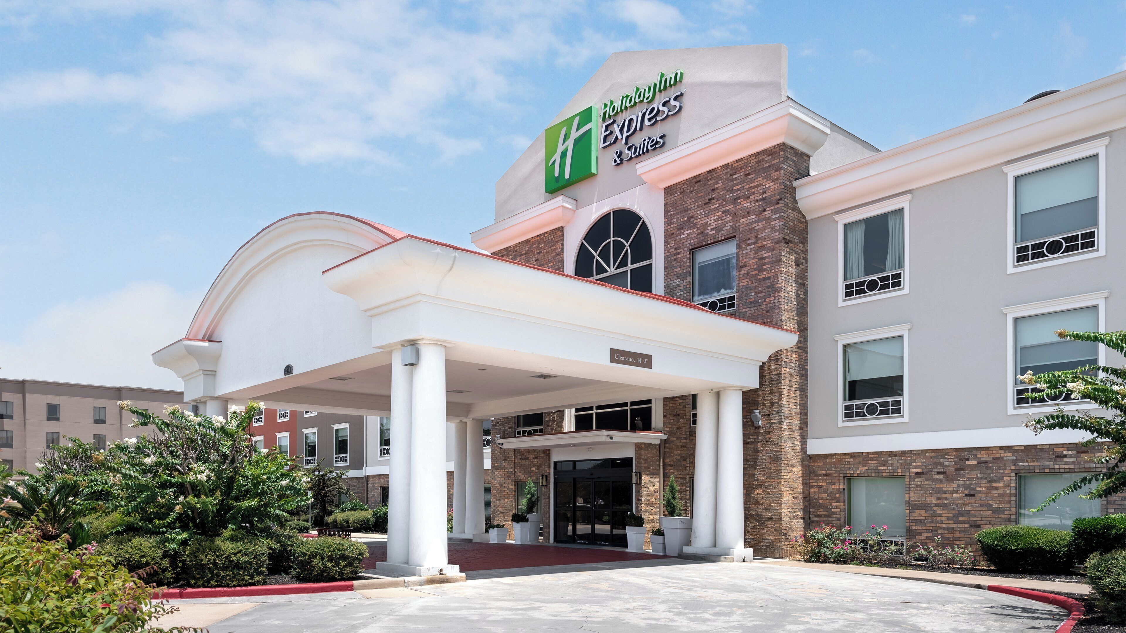 A Holiday Inn Express & Suites hotel with a covered entrance, brick facade, and a clear sky.