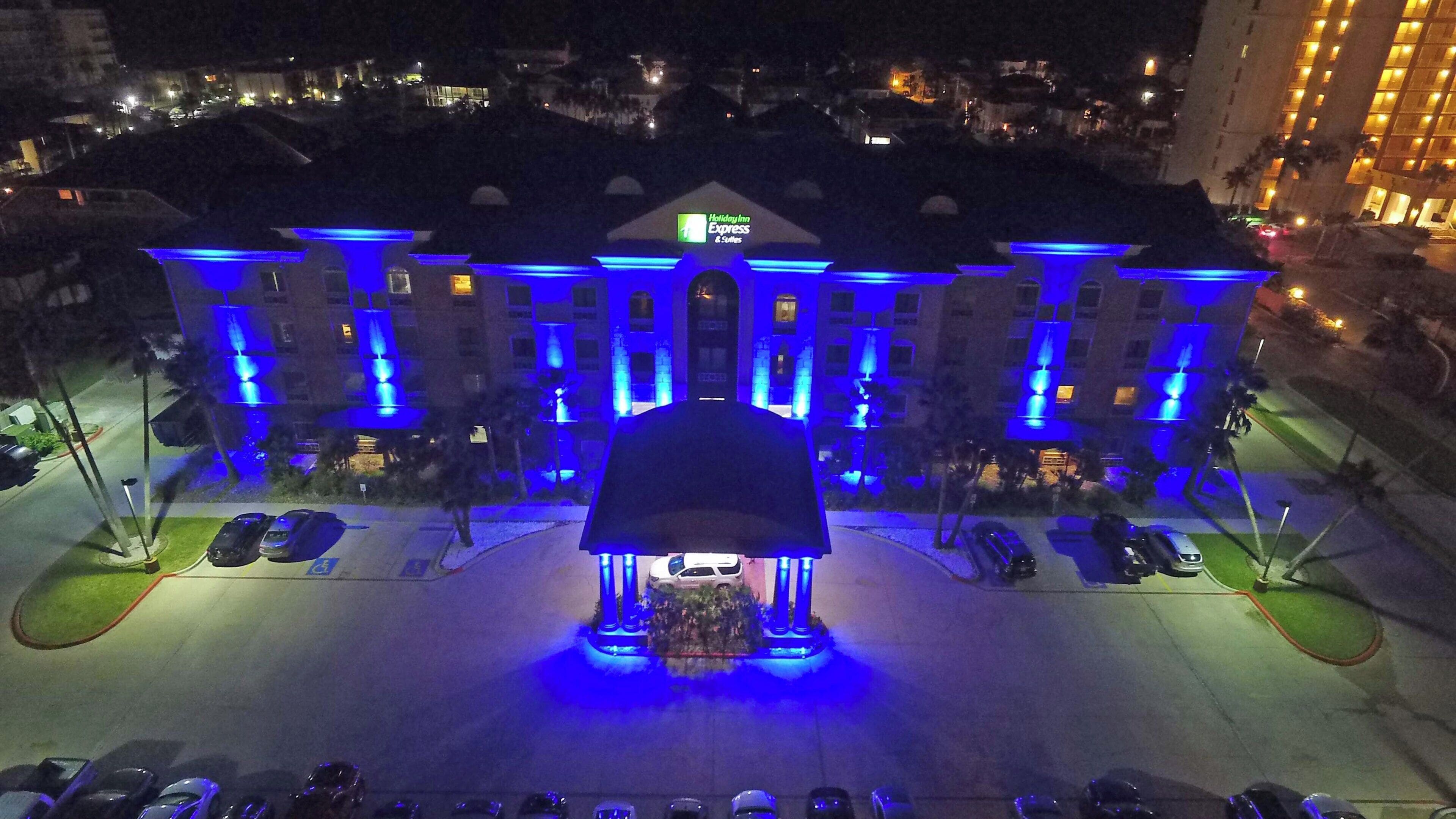 A hotel with a central entrance, multiple parking spaces, and a well-lit facade.