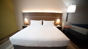 Una cama grande con cabecera de madera, dos mesitas de noche con lámparas y una pequeña mesa redonda con una silla.
