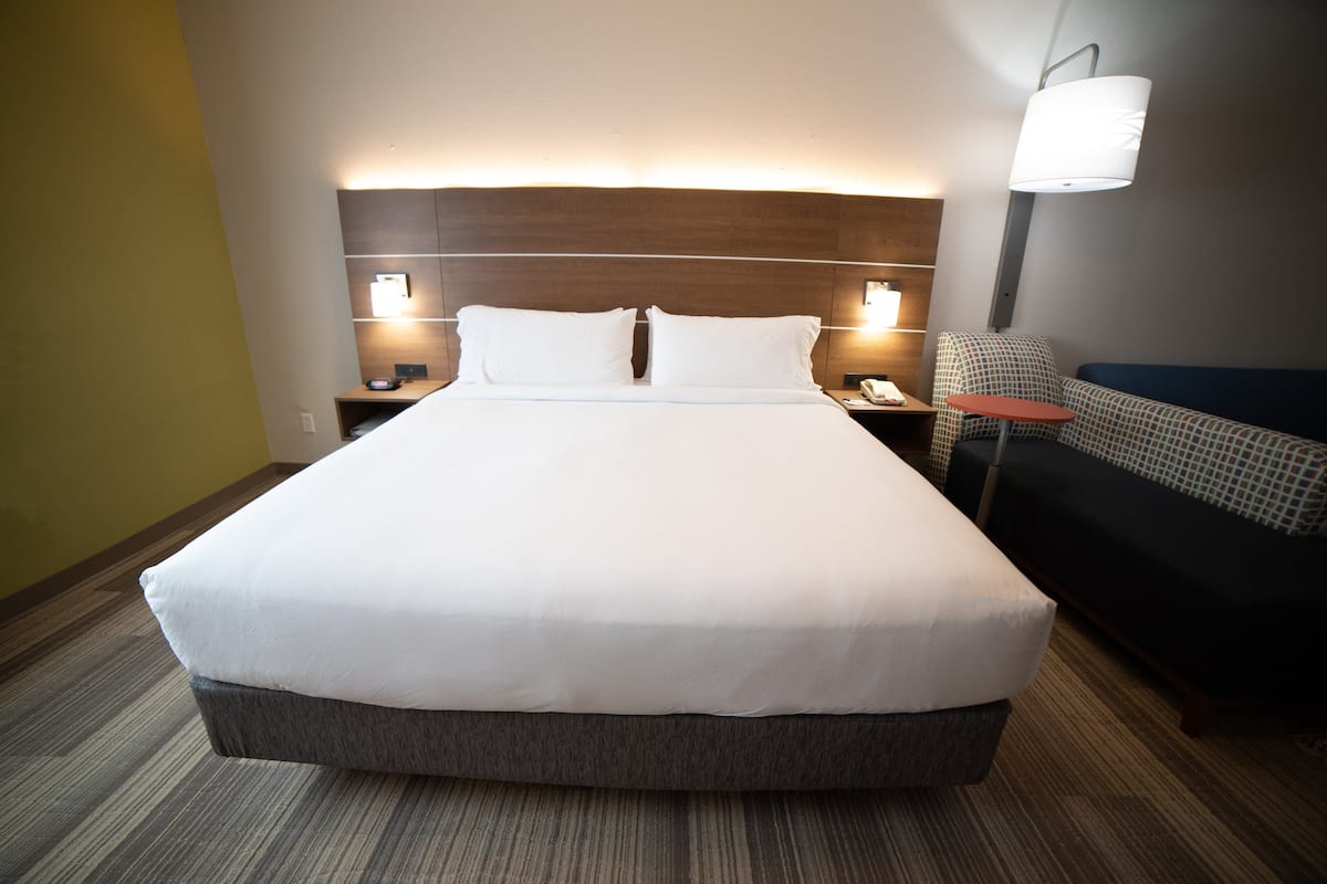 A large bed with a wooden headboard, two bedside tables with lamps, and a small round table with a chair.
