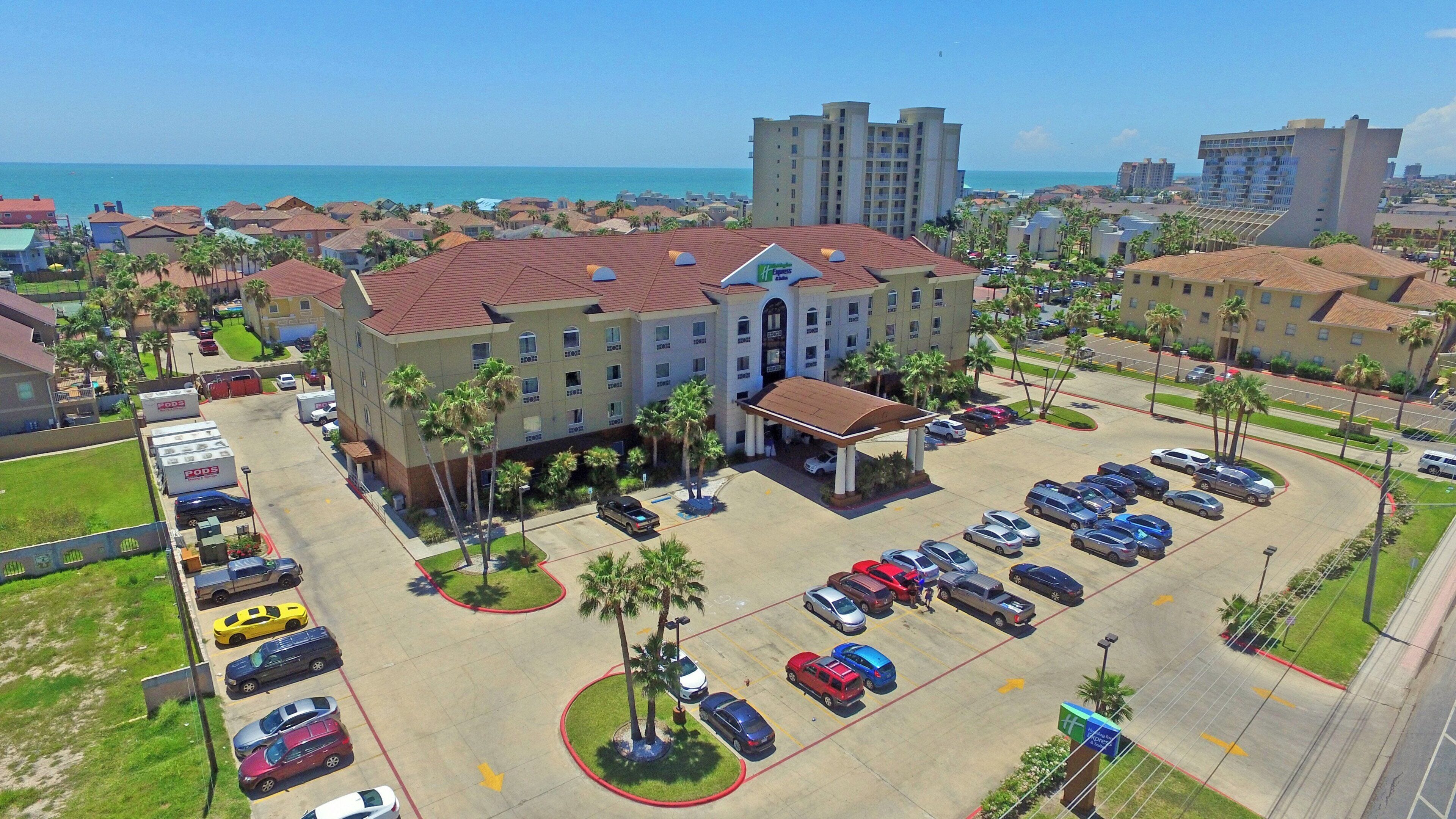 A hotel with a parking lot, a beach view, and a large building in the background.